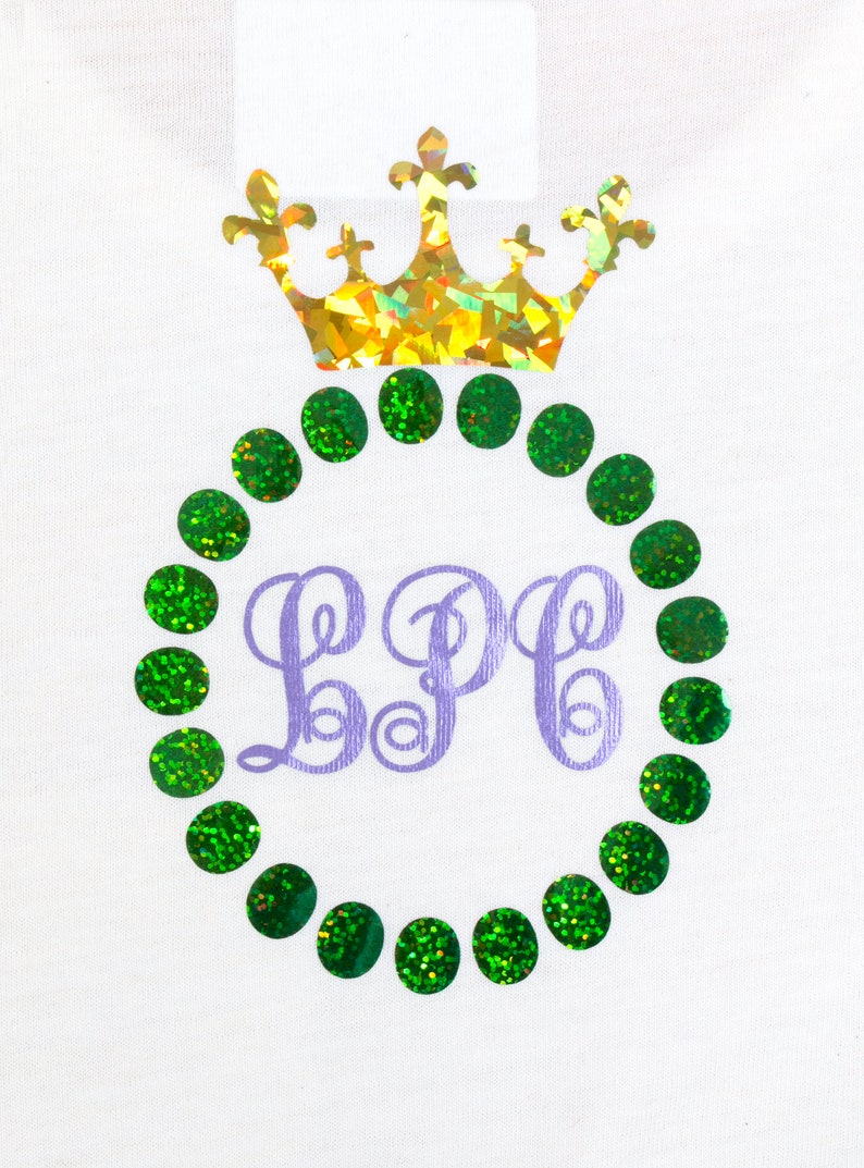 May include: A white t-shirt with a purple monogram "LPP" surrounded by a circle of green glitter dots. A gold glitter crown sits above the monogram.