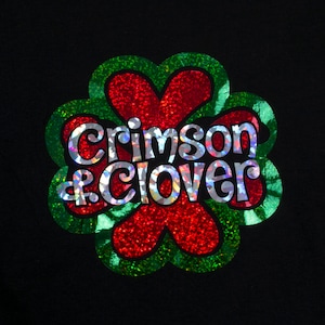 May include: A green four-leaf clover with a red center and the words "Crimson & Clover" in silver glitter.