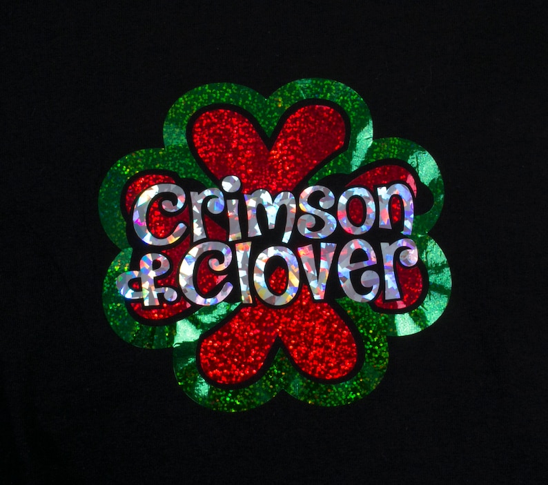 May include: A green four-leaf clover with a red center and the words "Crimson & Clover" in silver glitter.
