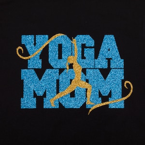 Op de afbeelding: Een zwart T-shirt met een blauw en gouden glitterontwerp met de tekst "Yoga Mom" en een silhouet van een vrouw die yoga doet in het midden van het woord "Mom".