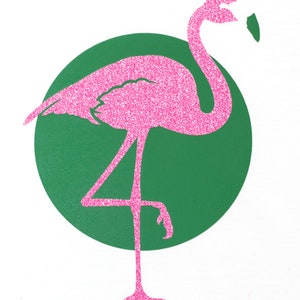 Op de afbeelding: Pink glitter flamingo silhouet staand op &eacute;&eacute;n been tegen een groene cirkel achtergrond.