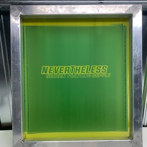 May include: A green screen printing frame with a yellow border. The frame has the text "NEVERTHELESS SCREEN PRINTING SUPPLY" printed on it.