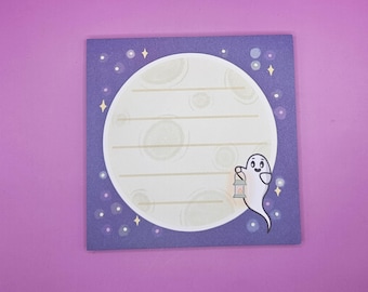 May include: Square notepad with a purple background and a large white moon design. A cartoon ghost holding a lantern is on the right side. The moon has horizontal lines for writing. Small white stars and dots are scattered around the moon.