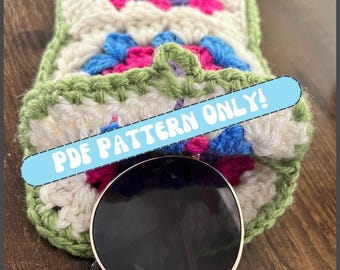 Pode incluir: Um estojo de óculos de sol de crochê feito à mão com um design de granny square. O estojo apresenta uma mistura de fios brancos, verdes, rosa, azuis e roxos. O texto "PDF PATTERN ONLY!" é exibido em uma faixa azul. Óculos de sol são parcialmente visíveis.