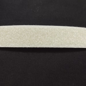 May include: Three handmade bunny dolls wearing different patterned dresses and hats. The bunny dolls are sitting on a green grassy surface.