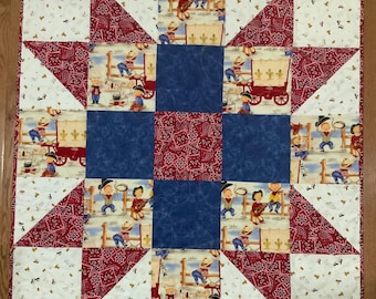 May include: A red, white, and blue patchwork quilt with a star design. The quilt features a central square with a blue background and a red and white paisley pattern. The surrounding squares feature cowboys and horses.