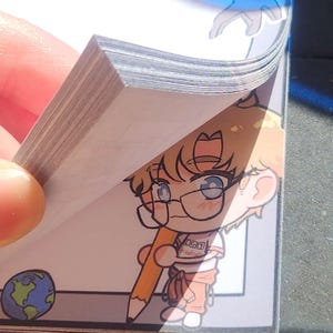 May include: A notepad with a stack of white paper sheets. Each sheet features a cartoon illustration of a light-haired character wearing glasses and holding a large yellow pencil. A small globe icon is in the bottom left corner.