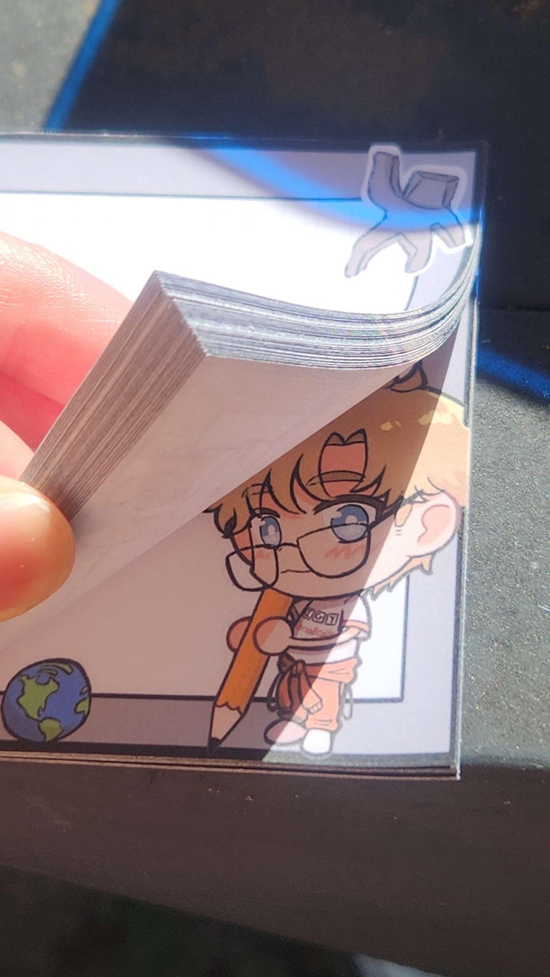 May include: A notepad with a stack of white paper sheets. Each sheet features a cartoon illustration of a light-haired character wearing glasses and holding a large yellow pencil. A small globe icon is in the bottom left corner.