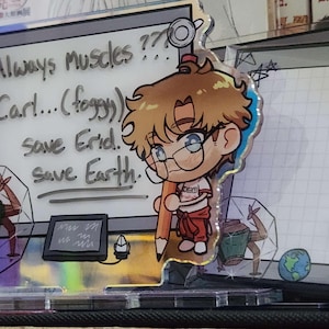 May include: An acrylic standee featuring a chibi character with brown hair and glasses holding a large pencil. The background panel displays a whiteboard with the text "Always muscles??? Carl...(foggy) save Erid. save Earth." and a small drawing of a planet.