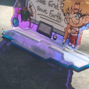 May include: An acrylic standee featuring a cartoon character with blonde hair and glasses holding a large pencil. The background panel displays the text: Always Muscles ??? Carl... (foggy) Save Erid. Save Earth. A small alien figure and a globe are also visible.