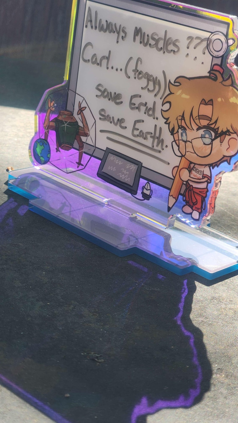 May include: An acrylic standee featuring a cartoon character with blonde hair and glasses holding a large pencil. The background panel displays the text: Always Muscles ??? Carl... (foggy) Save Erid. Save Earth. A small alien figure and a globe are also visible.
