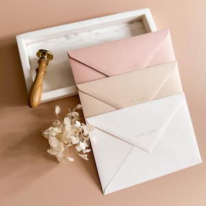 Könnte beinhalten: Drei pastellfarbene Umschläge in Rosa, Beige und Weiß, mit dem Aufdruck "with love". Ein Wachssiegel mit Holzgriff und Trockenblumen sind ebenfalls im Bild zu sehen.