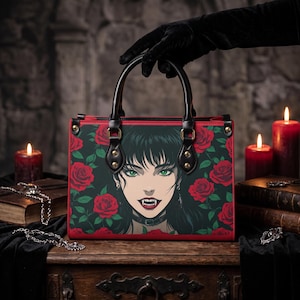 May include: A rectangular handbag featuring a dark green background with a pattern of red roses and a central illustration of a person with black hair, green eyes, and visible fangs. The bag has black leather handles and red trim.