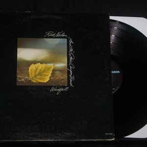 May include: A black vinyl record album cover titled Windfall by Rick Nelson and the Stone Canyon Band. The cover features a square central image of a single yellow leaf on the ground. A black vinyl record is partially pulled out of the sleeve.
