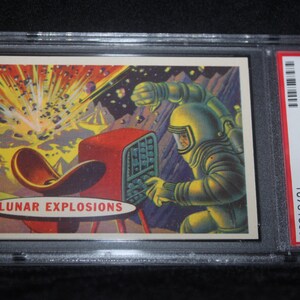 May include: A vintage trading card titled "1957 Target: Moon Lunar Explosions" featuring an astronaut in a yellow spacesuit operating a red console. The card shows a colorful illustration of a lunar explosion. The card is graded and encased in a protective holder.