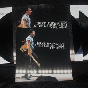May include: A black vinyl record album cover with a photo of Bruce Springsteen and the E Street Band. The album title is "Bruce Springsteen & The E Street Band Live/1975-85".