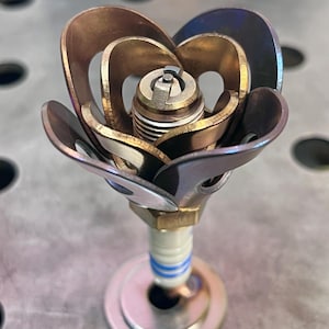 May include: A metal rose sculpture made from a spark plug and metal petals. The petals are a mix of gold and iridescent blue.