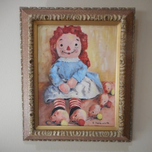 May include: A framed painting of a red-haired rag doll wearing a blue dress and red and white striped stockings. The doll is sitting on a yellow background with several small red and yellow balls scattered around her. The painting is signed "R. Haldenworth" in the lower right corner.
