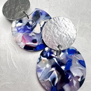 May include: A pair of silver and blue earrings with a textured silver disc and a blue and white marbled disc.