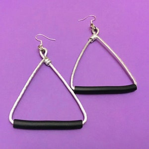 May include: A pair of silver triangle earrings with black rubber accents. The earrings are dangling and have a hook closure.