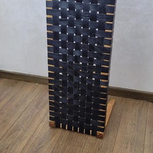 May include: A black leather woven side table with a wooden frame. The table is on a wood floor.