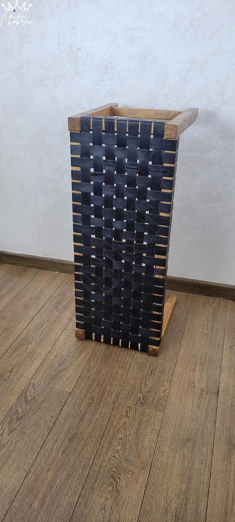 May include: A black leather woven side table with a wooden frame. The table is on a wood floor.