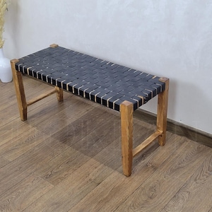 May include: A black leather bench with a woven design and wooden legs. The bench is sitting on a wooden floor.