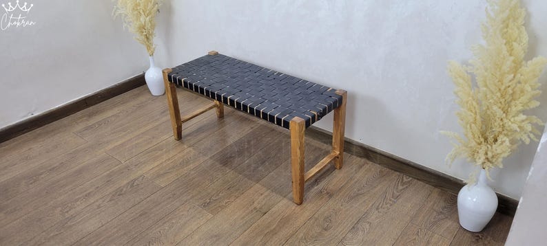 May include: A black leather bench with a woven design and wooden legs. The bench is sitting on a wooden floor.