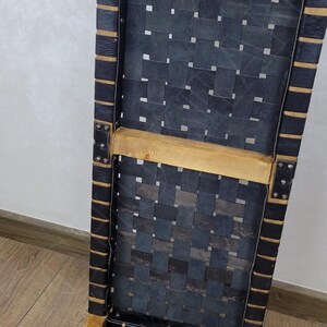 May include: A wooden chair with a black leather seat. The seat is woven in a grid pattern. The chair has a simple design with straight legs.