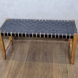 May include: A black leather bench with a woven design and wooden legs. The bench is sitting on a wooden floor.