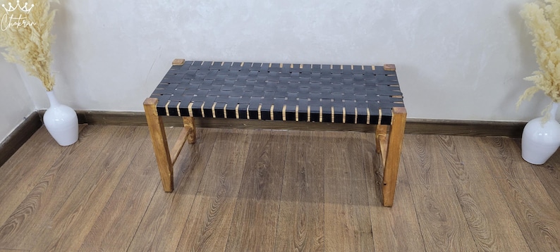 May include: A black leather bench with a woven design and wooden legs. The bench is sitting on a wooden floor.