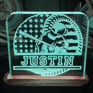 May include: A green and white personalized night light with a baseball player silhouette and an American flag design. The name "JUSTIN" is engraved below the image.
