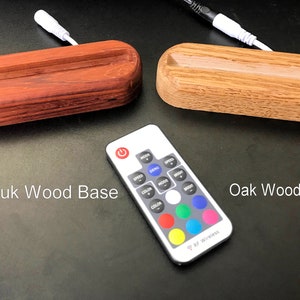 May include: Two wooden bases for a phone stand, one is made of Padauk wood and the other is made of Oak wood. A remote control with buttons for color, speed, and mode is in the center of the image.