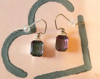May include: A pair of silver earrings with iridescent purple and green square-shaped glass stones.