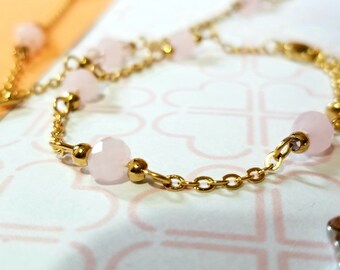 Könnte beinhalten: Ein goldenes Kettenarmband mit rosa Perlen. Das Armband hat eine zarte Kette und ist mit kleinen, runden rosa Perlen verziert.