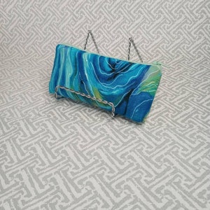 May include: A blue and green zippered pouch with a swirling abstract pattern. The pouch is on a white background with a geometric pattern.