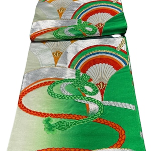 May include: A decorative Japanese obi sash featuring a fan and landscape design. The sash has a green, silver, and orange color scheme. The design includes fans, mountains, and decorative rope elements.