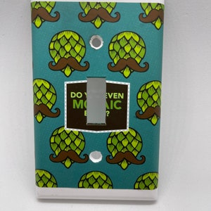 May include: A light switch cover with a teal background and a repeating pattern of green hops and brown mustaches. The text "Do you even Mosaic?" is printed on the switch plate.