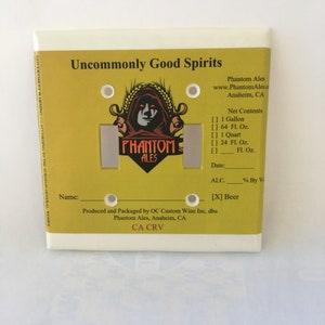 May include: A yellow and white light switch cover with the text "Uncommonly Good Spirits" and a logo of a phantom with the text "Phantom Ales". The switch cover also includes information about the product, including the net contents, alcohol content, and the producer.