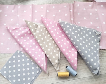 May include: Four pieces of fabric with white polka dots on a pink, beige, and gray background. The fabric is folded into triangles and arranged on a wooden surface. Two spools of thread are also visible on the surface.