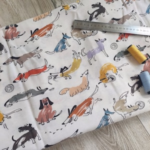 May include: White fabric with a repeating pattern of colorful cartoon dogs in various poses. The dogs are drawn in a whimsical style with different colors and patterns.