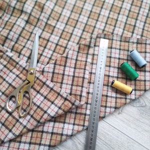 May include: A beige, brown, and white plaid fabric with a ruler, scissors, and spools of thread in blue, green, and yellow.