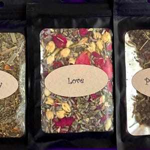 Puede incluir: Tres bolsas negras que contienen hierbas y flores secas. La bolsa de la izquierda est&aacute; etiquetada como Prosperity, la central como Love y la de la derecha como Protection. Cada bolsa tiene una ventana transparente con el contenido.