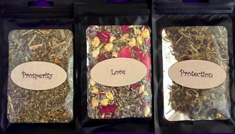 Puede incluir: Tres bolsas negras que contienen hierbas y flores secas. La bolsa de la izquierda est&aacute; etiquetada como Prosperity, la central como Love y la de la derecha como Protection. Cada bolsa tiene una ventana transparente con el contenido.