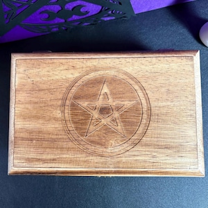 May include: A rectangular wooden box with a carved pentagram design inside a circle on the lid. The box is made of light brown wood and has a simple, classic design. The box is closed and appears to be new.