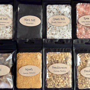 Puede incluir: Ocho bolsas negras con ventanas transparentes que contienen diversas sales y resinas. Las etiquetas incluyen Herbal Salt, Black Salt, Green Salt, Rose Salt, Copal, Myrrh y Frankincense, cada una con texto descriptivo en pegatinas ovaladas.