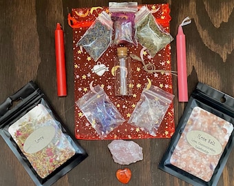 May include: A red and pink love spell kit with a red candle, pink candle, rose quartz crystal, love salt, herbs, and a small glass bottle. The kit is packaged in a red mesh bag with stars and moons.