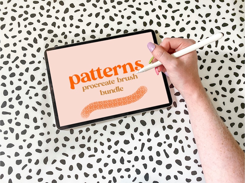 May include: A digital tablet displaying the text "patterns procreate brush bundle" in orange and gold text on a pink background. A hand is holding a white stylus and drawing a pattern on the screen.