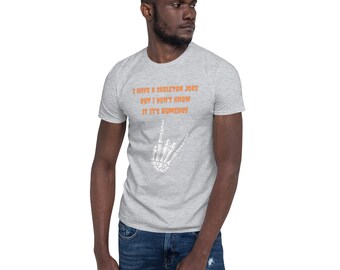 Può includere: Una t-shirt grigio melange a maniche corte con il testo arancione I HAVE A SKELETON JOKE BUT I DON'T KNOW IF IT'S HUMERUS e una grafica bianca di una mano scheletrica che fa un gesto rock and roll sulla parte anteriore.