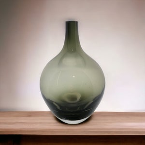 May include: A dark grey glass vase with a rounded body and a narrow neck. The vase is sitting on a wooden surface.